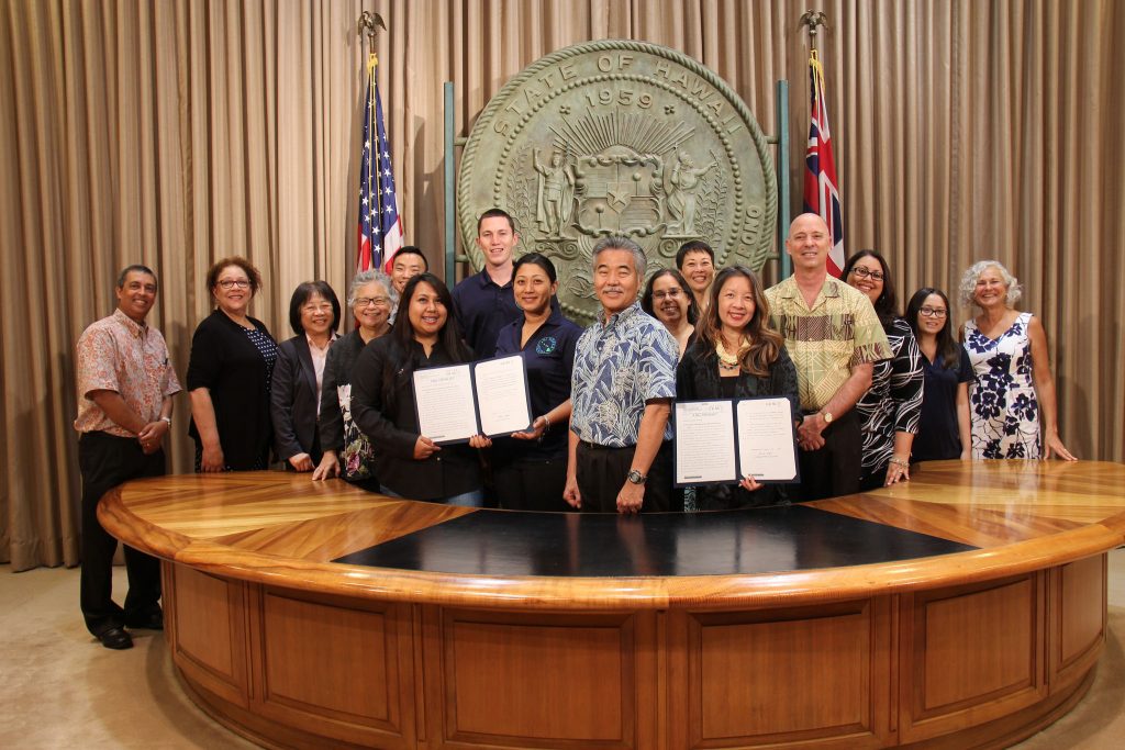 Gov. Ige stands beside young people, legislators, community members, DHS staff and other state employees after signing HB2350 and SB2878 into law. 